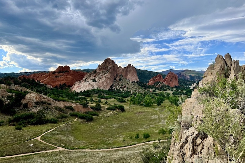 Red sandstone formations at Garden of the Gods in Colorado Springs under a cloudy sky, with green valley trails