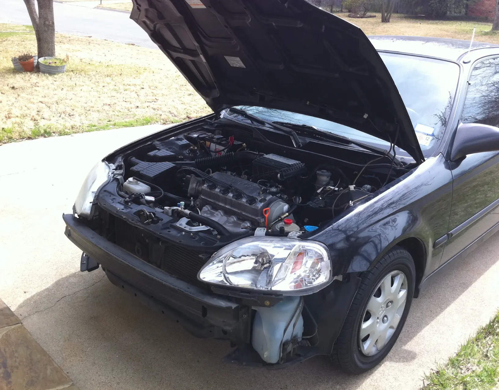 Keith Brown's old black Honda in a driveway with the hood up and the front bumper off during a repair