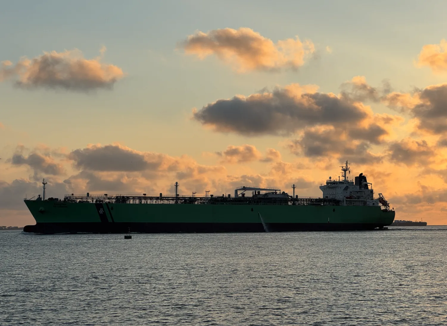 A large green oil and chemical tanker sailing past at sunrise off the Texas coast, under orange and grey clouds