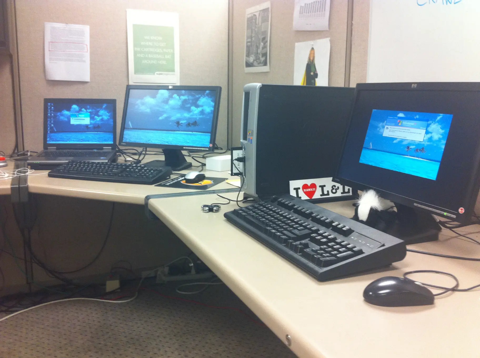 Keith Brown's Superpages.com cubicle with a laptop, two monitors and a desktop computer, under a Superpages poster