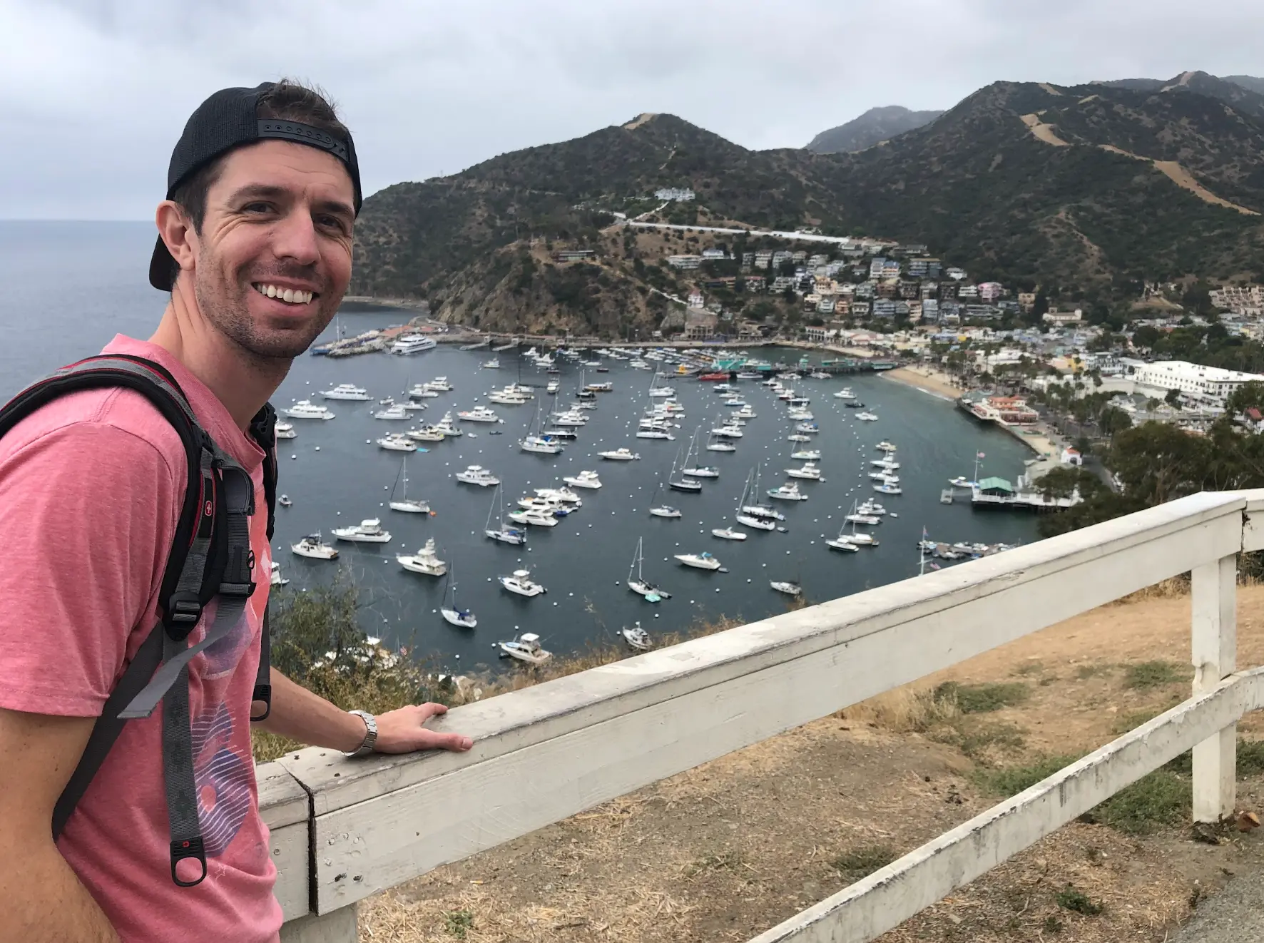 Keith Brown smiling at a lookout above the harbor on Catalina Island, with boats moored below