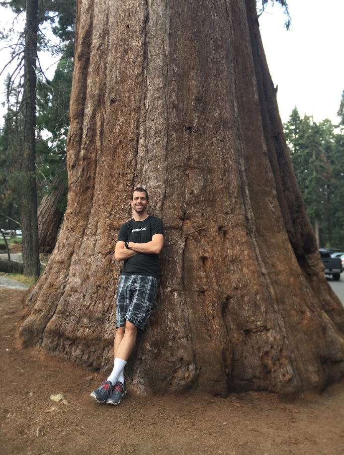 Keith Brown leaning against the trunk of a giant sequoia tree