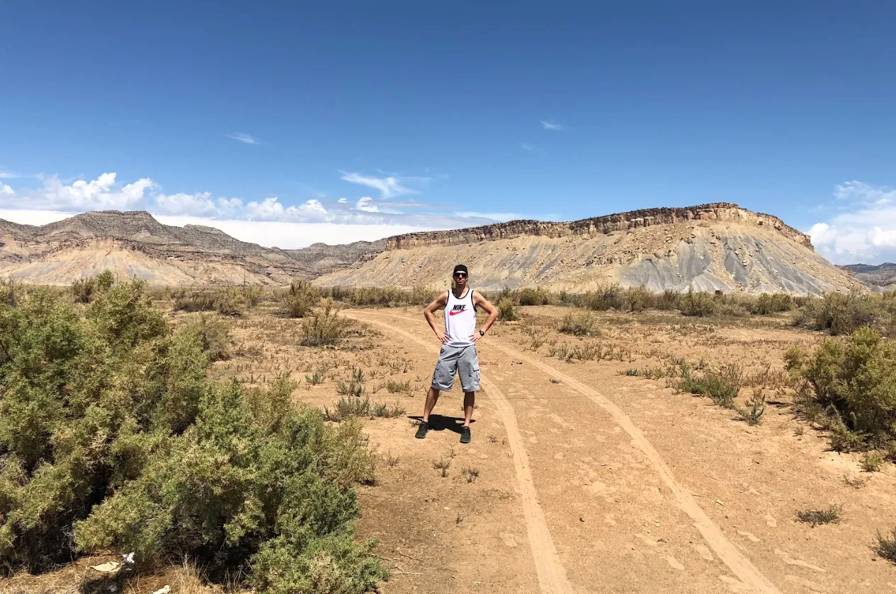 Keith Brown standing on a two-track dirt road in the desert with a flat-topped mesa behind him